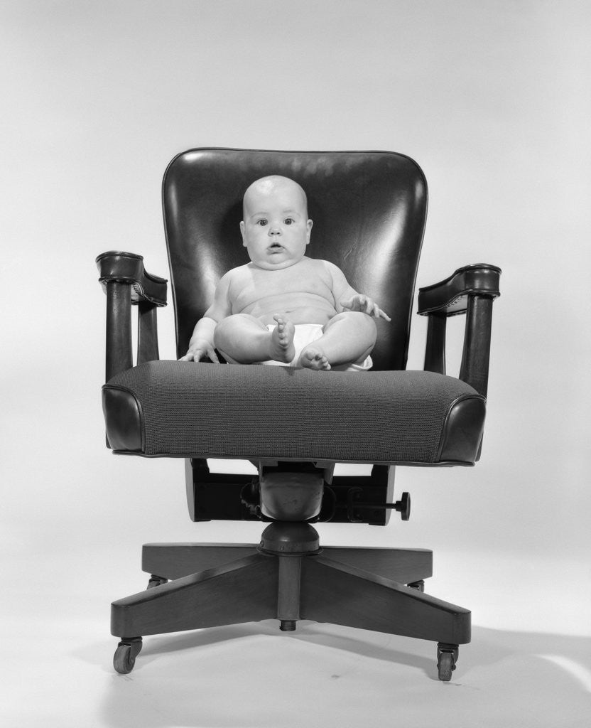 Detail of 1960s baby sitting in executive office chair looking at camera by Anonymous