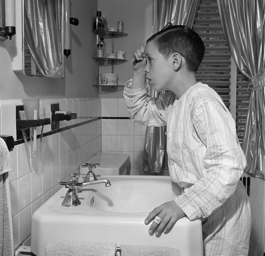 1950s boy combing hair looking in bathroom sink mirror by Corbis