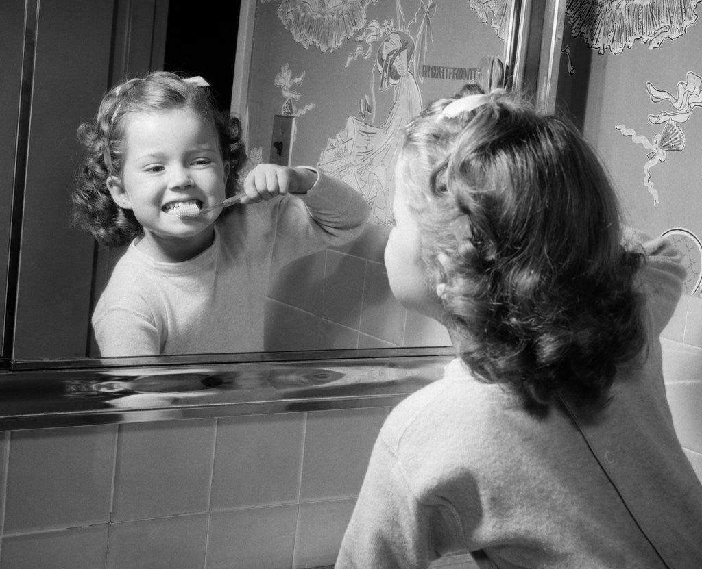 Detail of 1950s girl looking in bathroom mirror brushing teeth by Anonymous