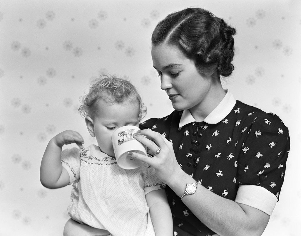 Detail of 1930s woman mother giving baby daughter drink from mug by Anonymous