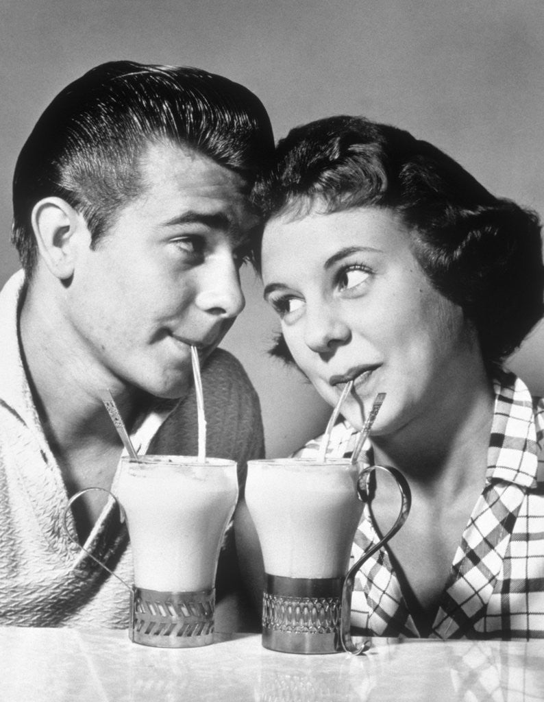 Detail of 1940s 1950s romantic teenage couple boy and girl head to head drinking ice cream sodas by Anonymous
