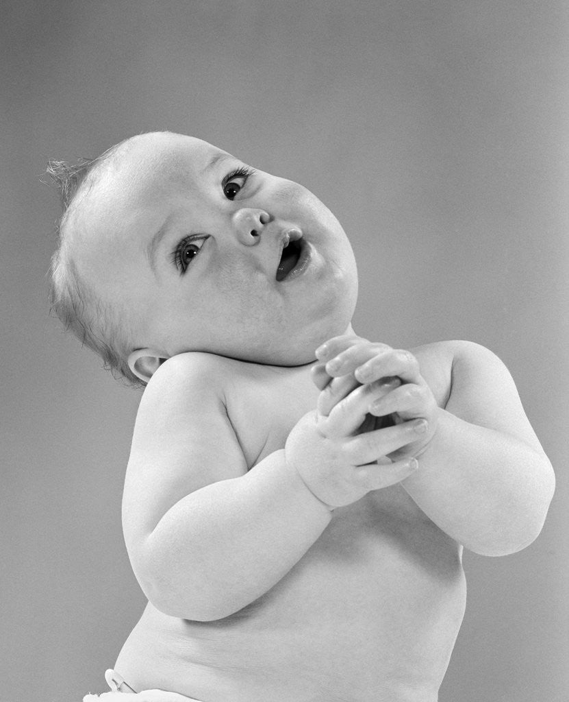 Detail of 1950s baby in diaper head to one side arms hands clasped in front by Anonymous
