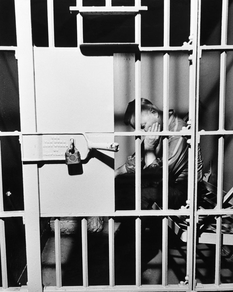 Detail of 1960s man seated on bench in jail cell with head in hand looking downward by Anonymous