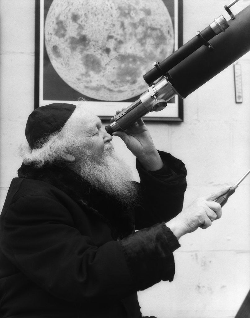 Detail of 1930s old astronomer white hair and beard wearing skull cap looking through telescope by Anonymous