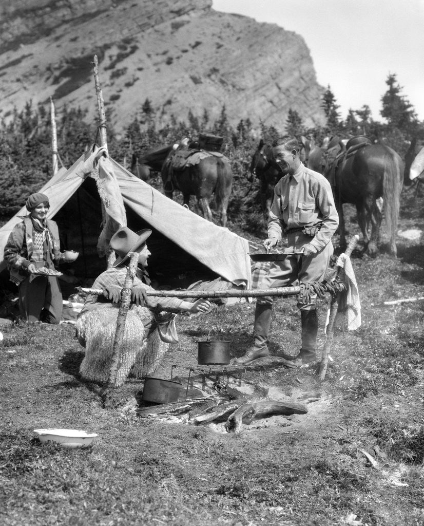 Detail of 1920s 1930s two men and one woman eating a meal around a campfire with a tent and horses at baker lake alberta canada by Anonymous