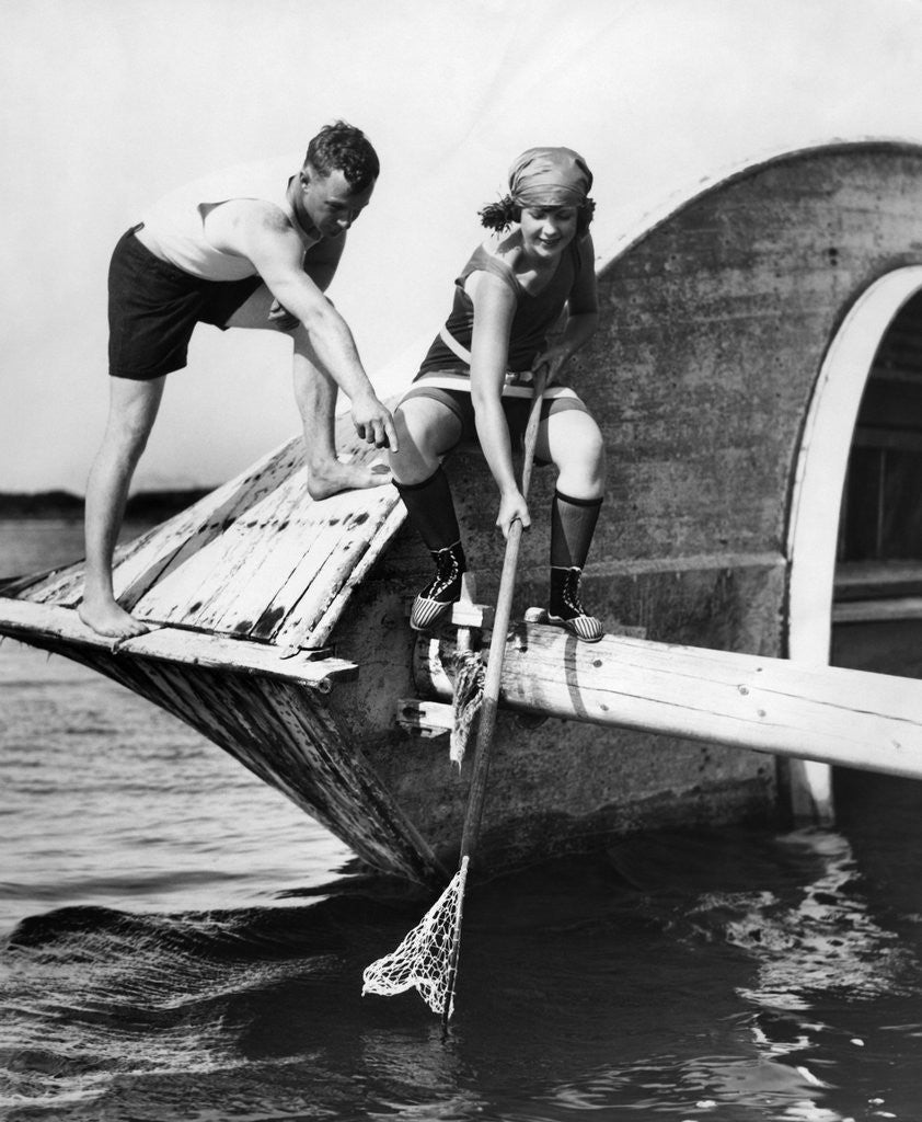Detail of 1920s man and woman in bathing suits crabbing off old abandoned wooden boat by Corbis