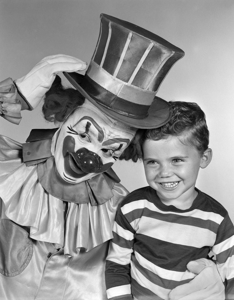 Detail of 1950s smiling clown with top hat arm around grinning boy in striped shirt by Corbis