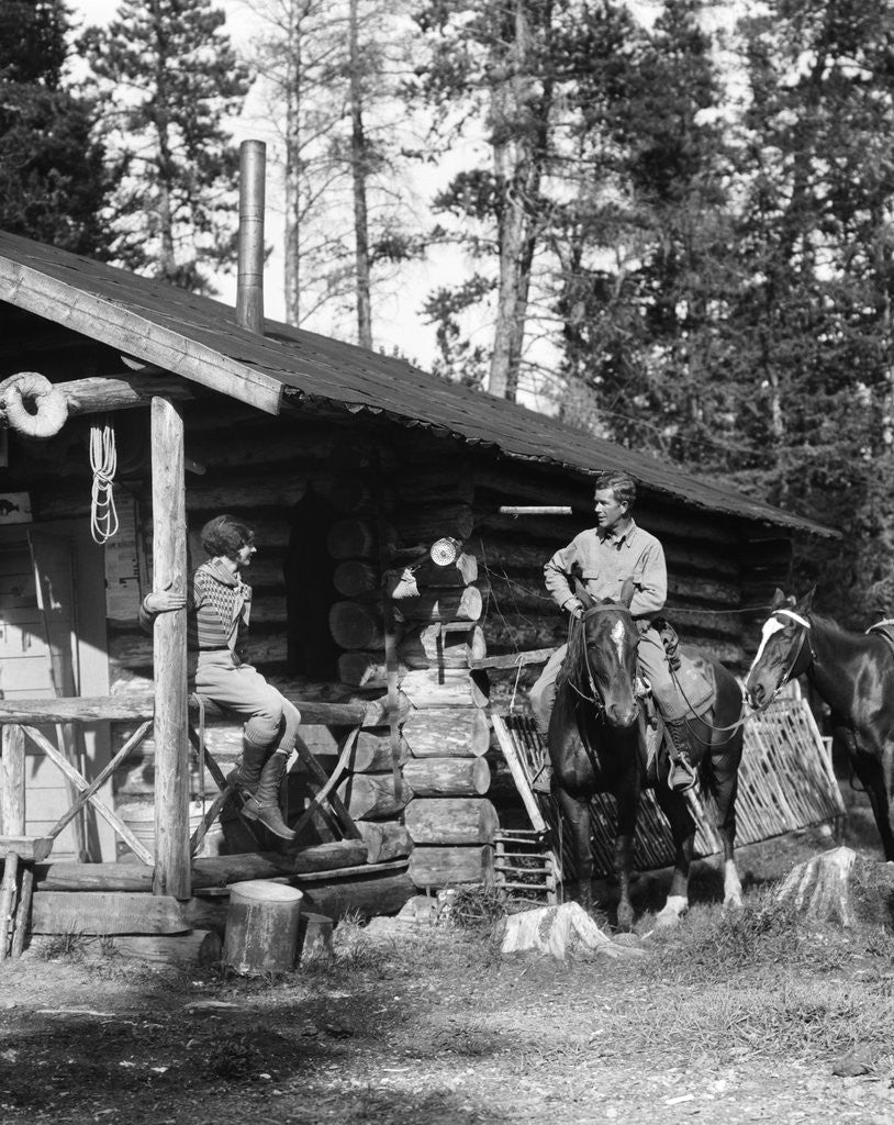 Detail of 1920s 1930s couple in front of log cabin woman sitting on porch railing man on horse alberta canada by Anonymous
