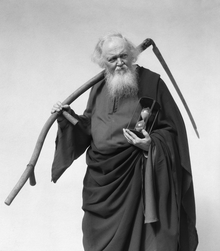 Detail of 1930s elderly white-bearded man in long robe carrying scythe and hourglass by Corbis