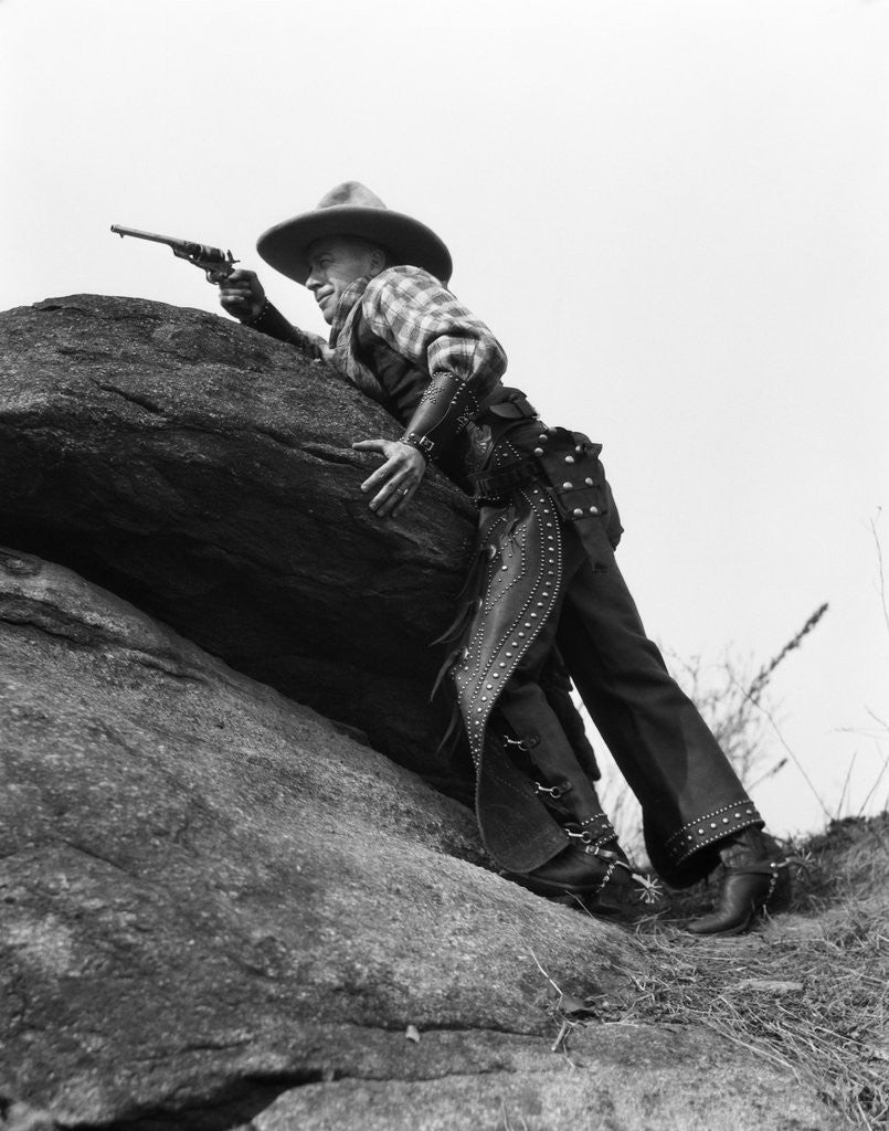 Detail of 1920s cowboy among rocks aiming revolver by Anonymous