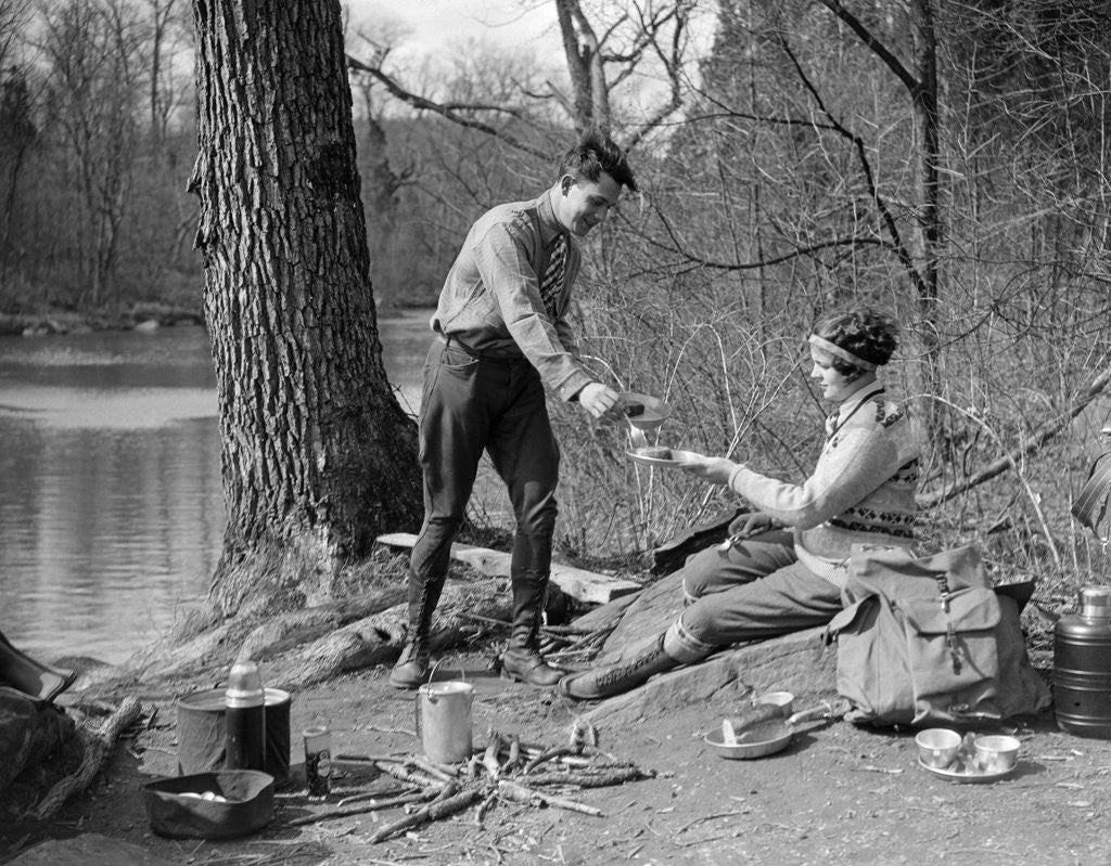 Detail of 1920s 1930s man & woman camping by lake having picnic woman sitting man standing serving food to woman east creek swamp by Anonymous