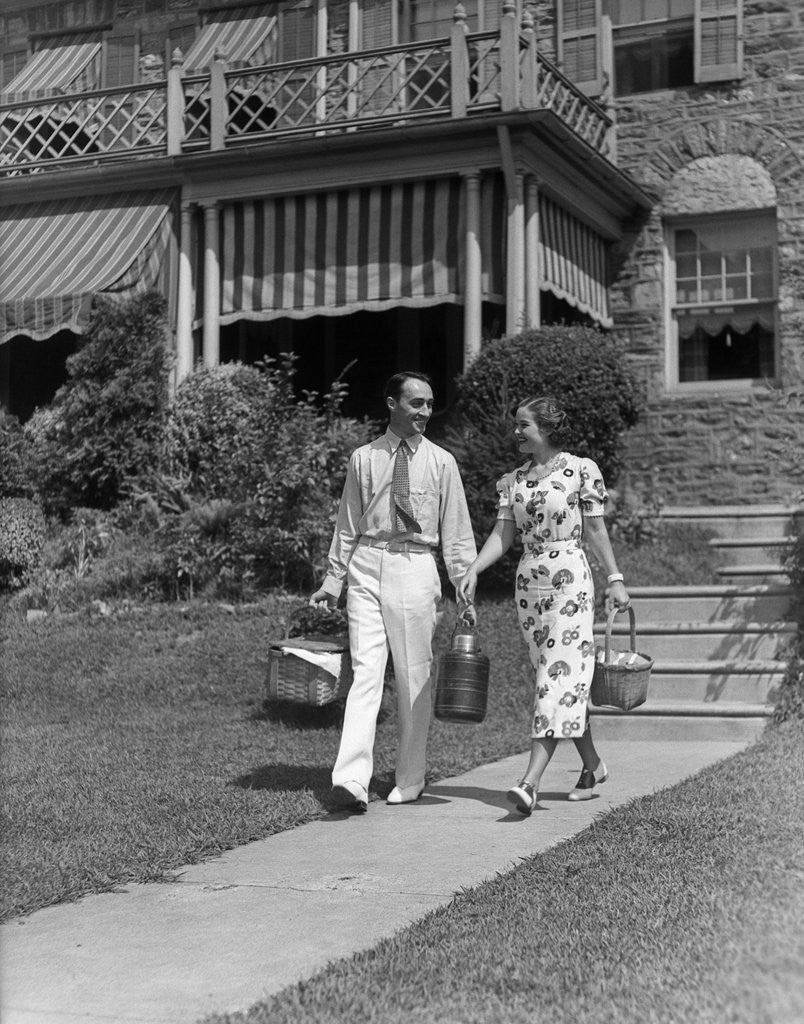 Detail of 1930s couple walking out of house down sidewalk carrying picnic baskets & thermos jug by Anonymous