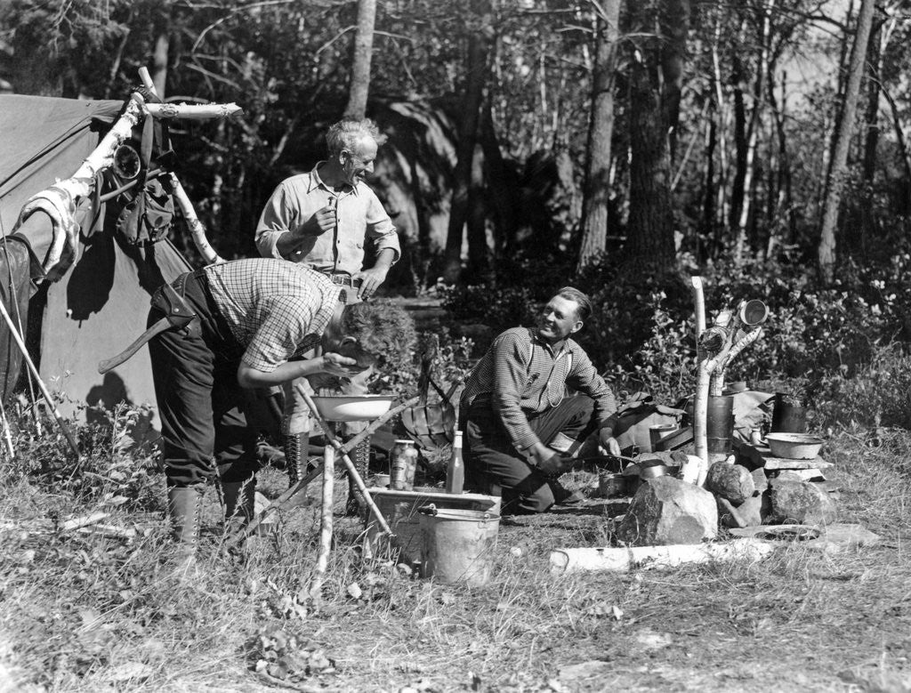 Detail of 1930s three men at campsite one washing his face at tripod wash stand the other tending campfire lake of the woods ontario canada by Anonymous