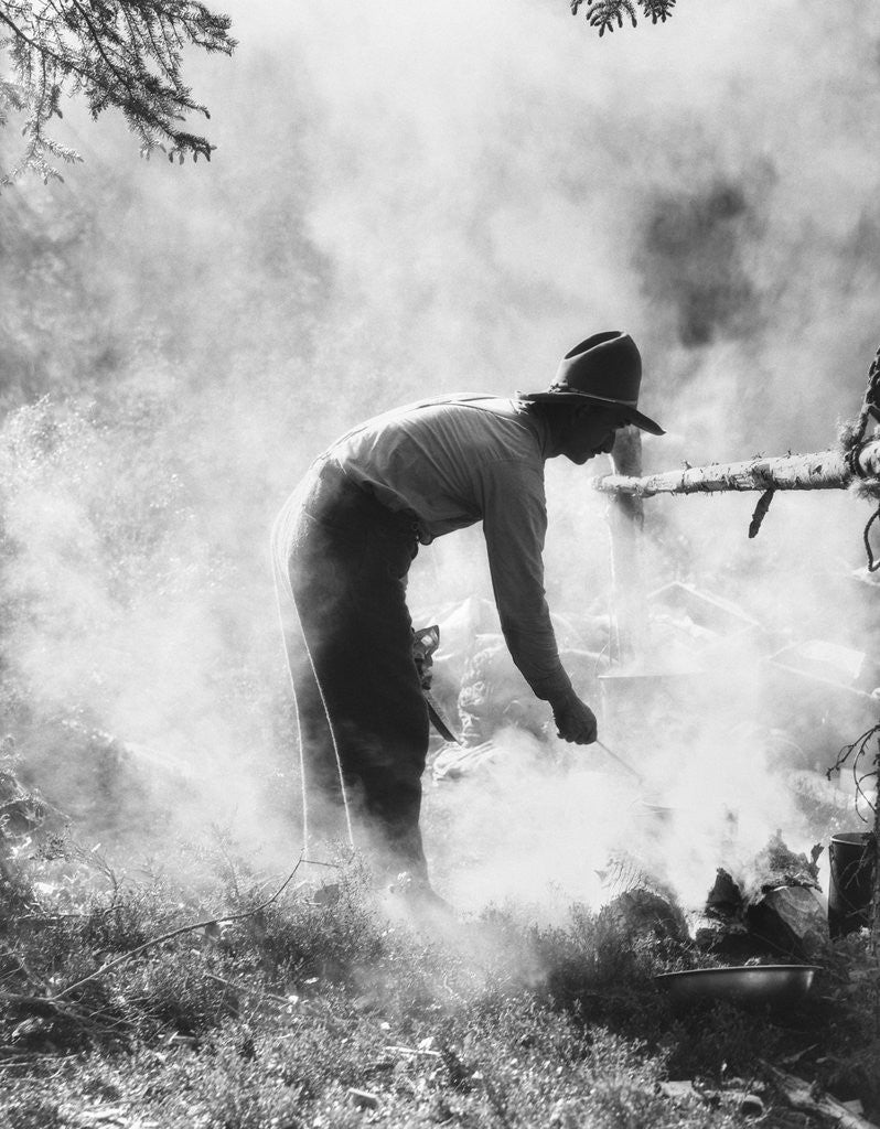 Detail of 1920s 1930s man cowboy cook bending over campfire by Anonymous