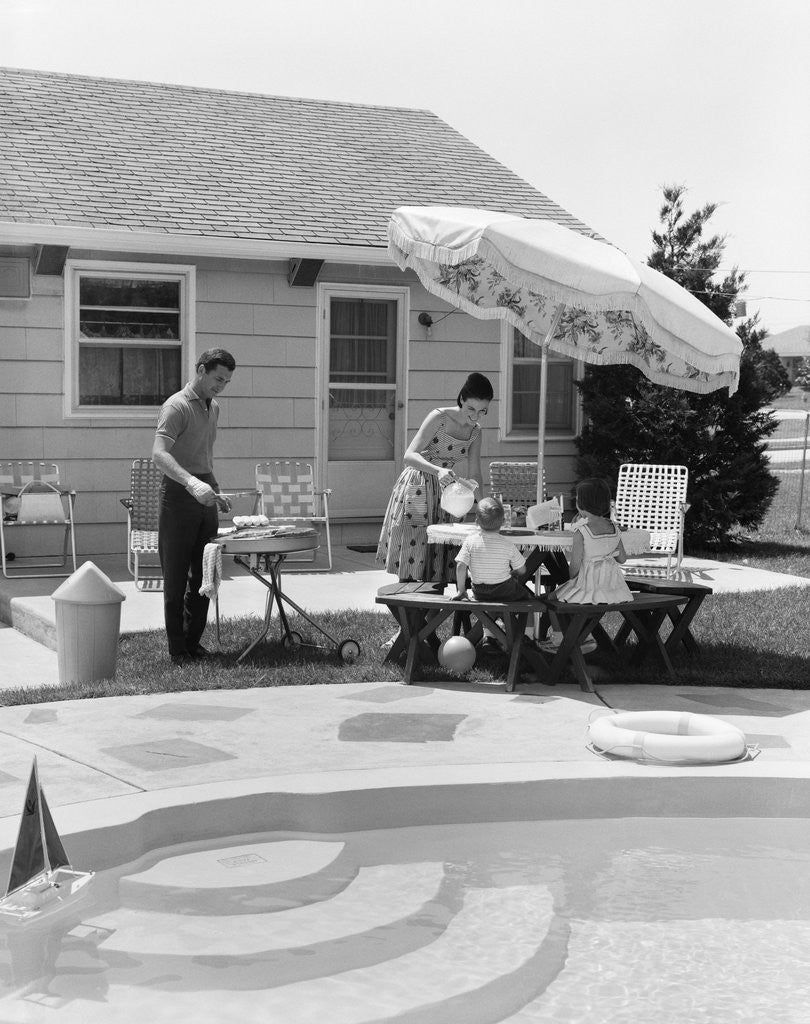 Detail of 1960s summer outdoor family of four backyard barbeque by pool father grilling mother serving lemonade to son and daughter by Corbis