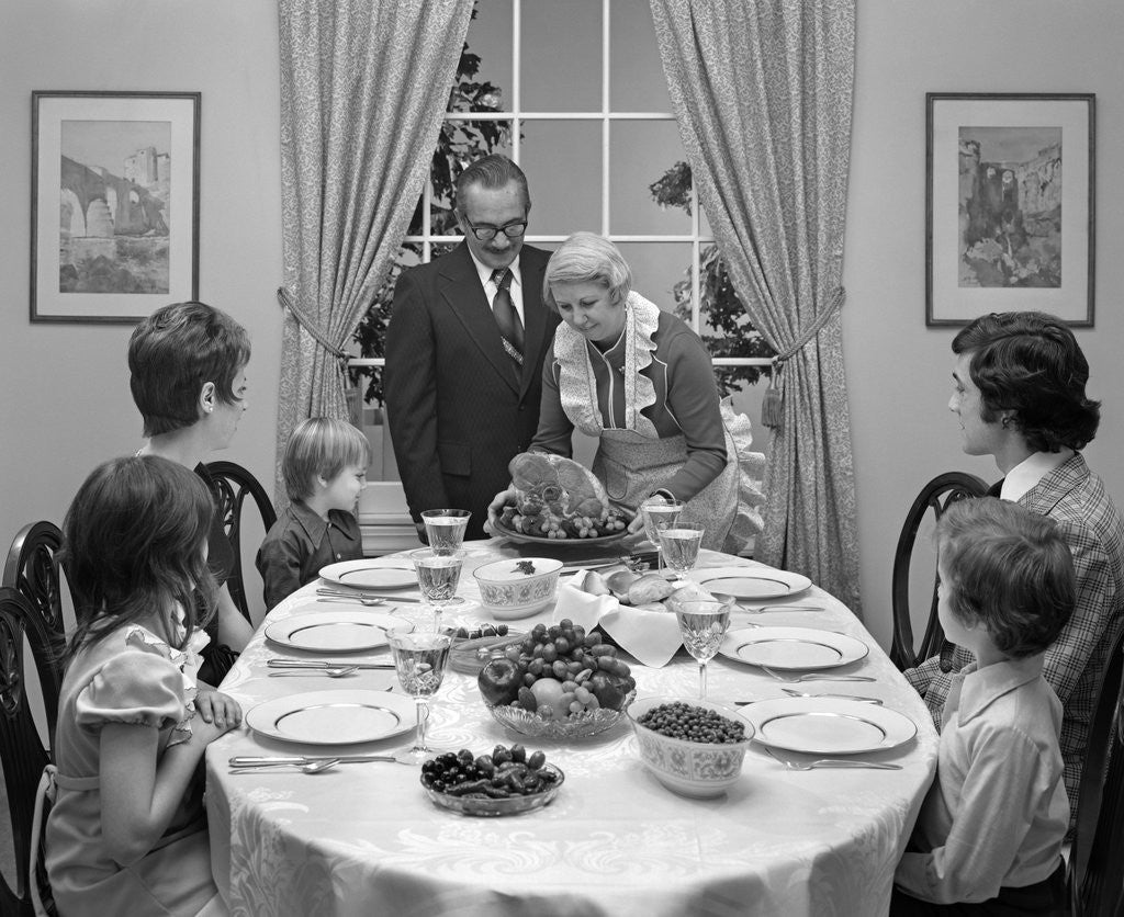 Detail of 1970s three generation family sitting around dining room table with grandmother serving a baked ham by Anonymous