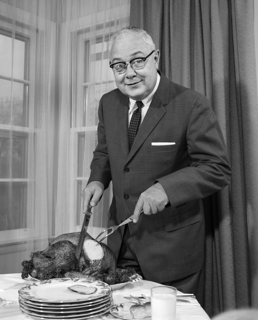 Detail of 1960s man carving thanksgiving roast turkey dinner looking at camera by Corbis