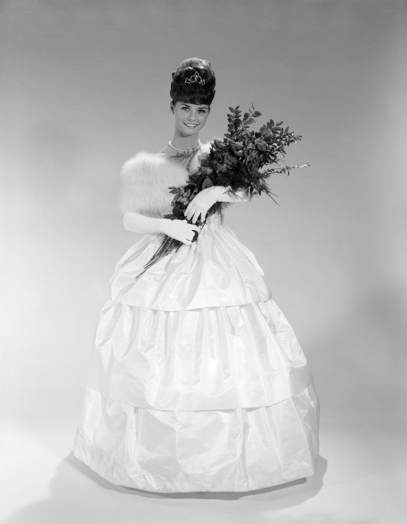 1960s pretty young woman in evening dress at beauty pageant wearing fur stole and tiara holding bouquet of roses looking at camera