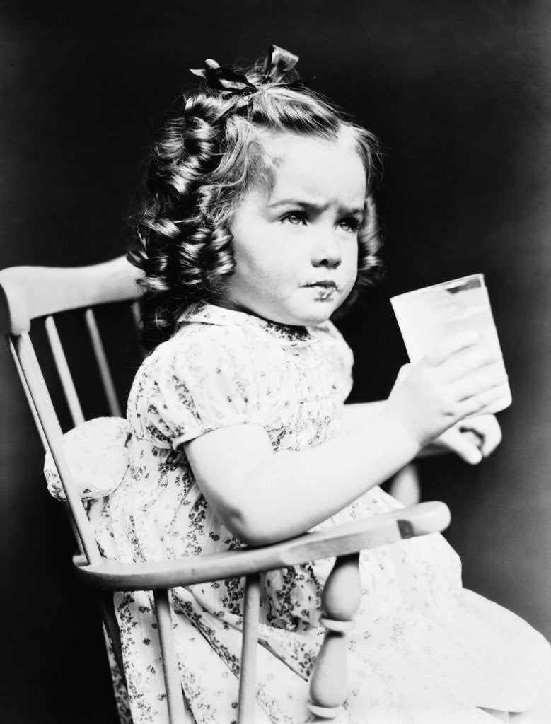 Detail of 1930s child girl sitting in high chair holding glass of milk serious look bow in hair baloney curls by Anonymous