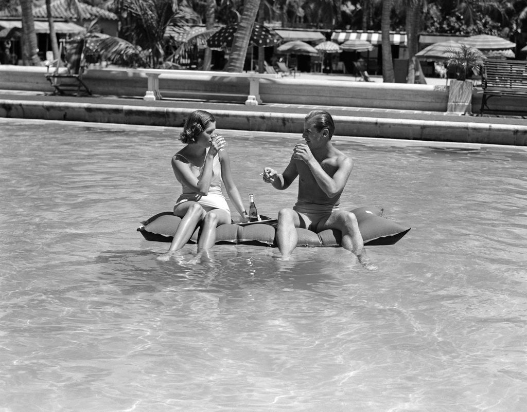 Detail of 1930s 1940s couple drinking while floating in a pool on a rubber raft at florida resort by Anonymous