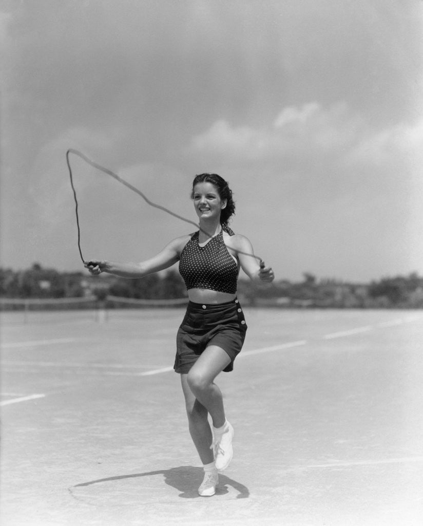 Detail of 1930s woman jumping rope exercise outdoors wearing polka dot halter top and shorts by Corbis