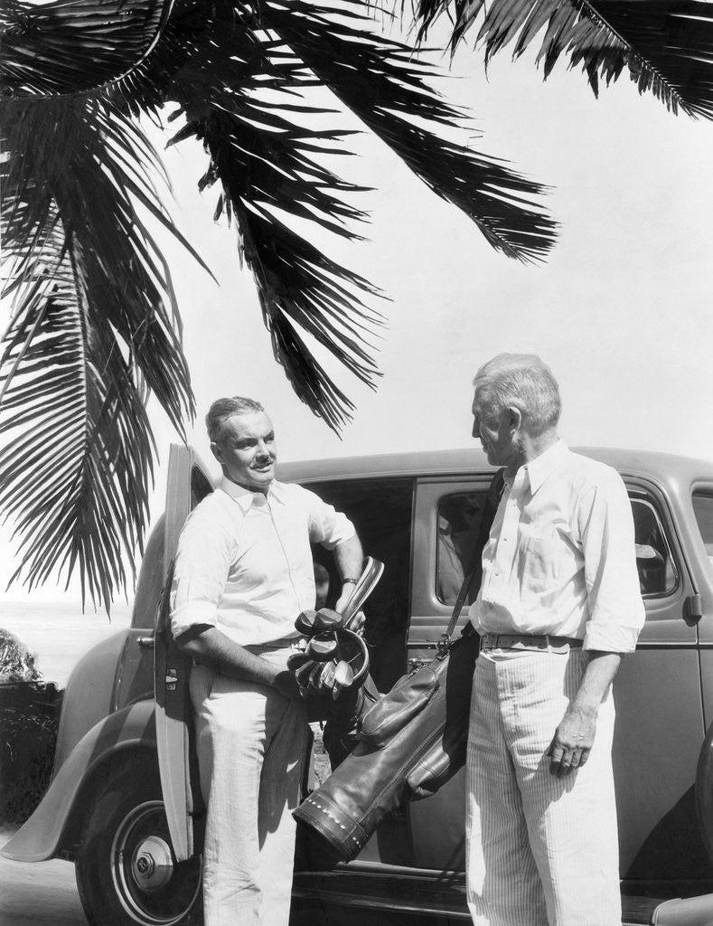 Detail of 1930s 2 elderly men standing by car carrying golf bag palm tree frond in corner by Anonymous
