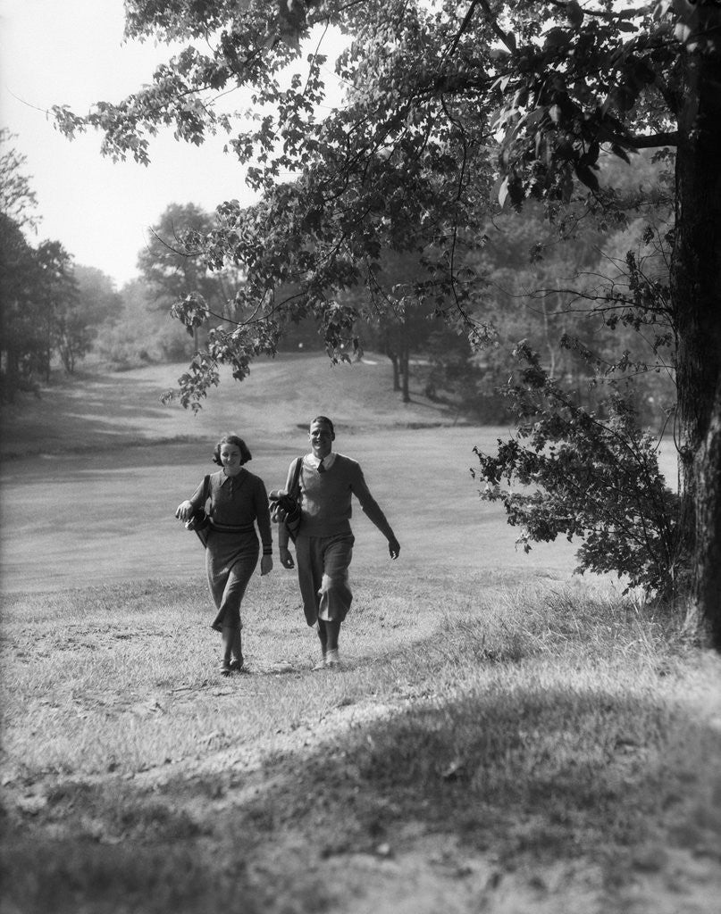 Detail of 1930s couple man woman each carrying a golf bag walking down the fairway of the golf course by Anonymous