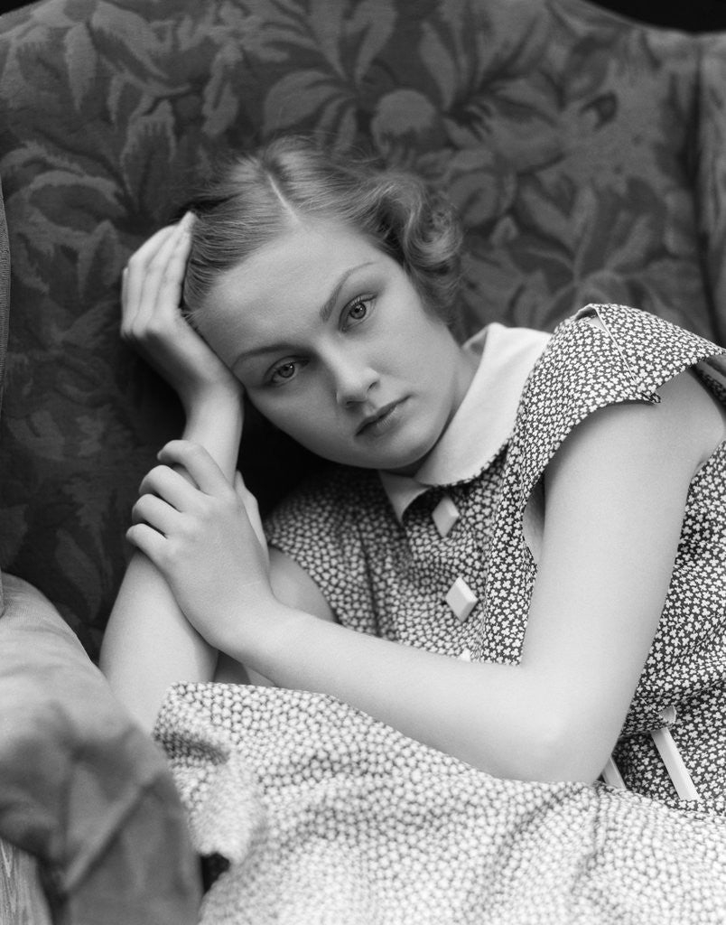 Detail of 1930s woman moping looking sad or depressed or with a headache leaning her head on her hand looking at camera by Anonymous