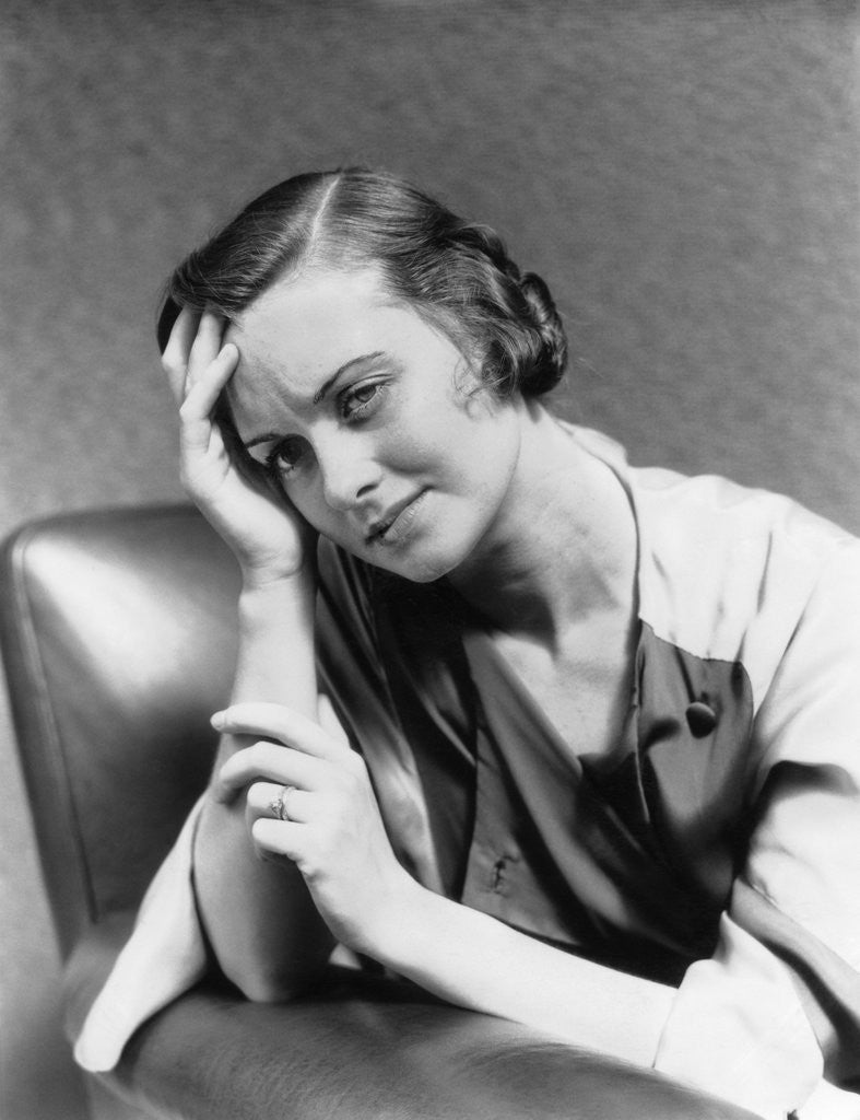 Detail of 1930s 1940s woman sitting in chair worried sad expression one hand up to her forehead by Anonymous