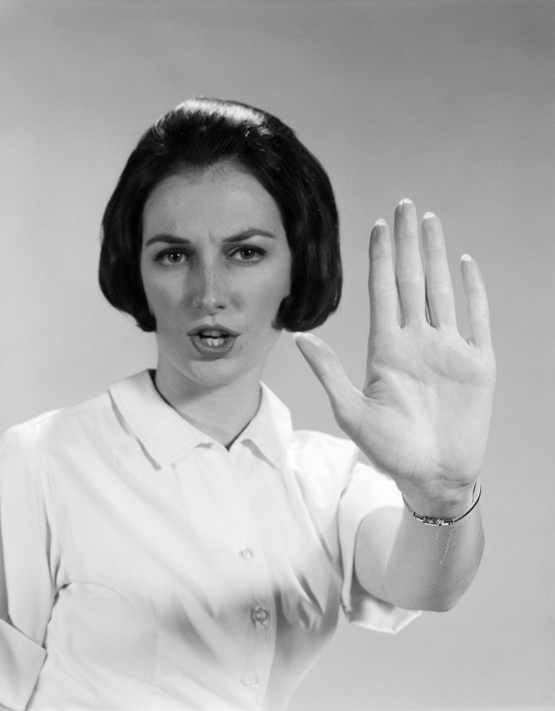 Detail of 1960s woman looking at camera holding up hand palm forward commanding stop by Anonymous
