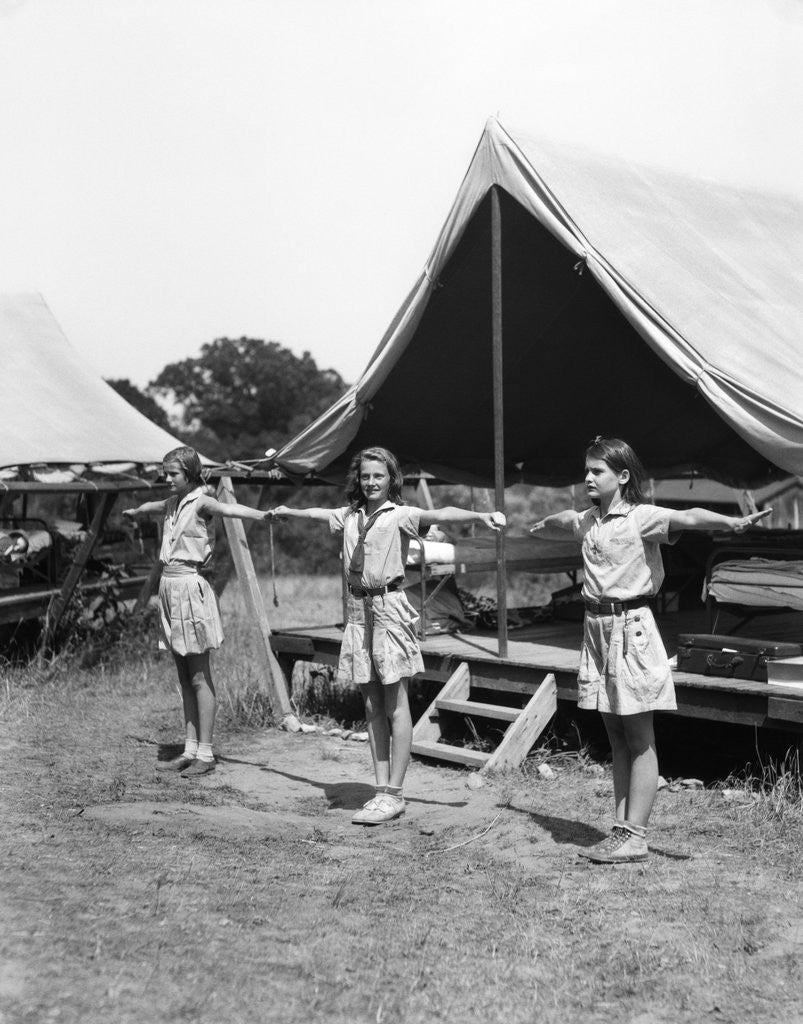 Detail of 1930s three teen girls doing exercise in a row with arms extended by tent summer camp by Anonymous