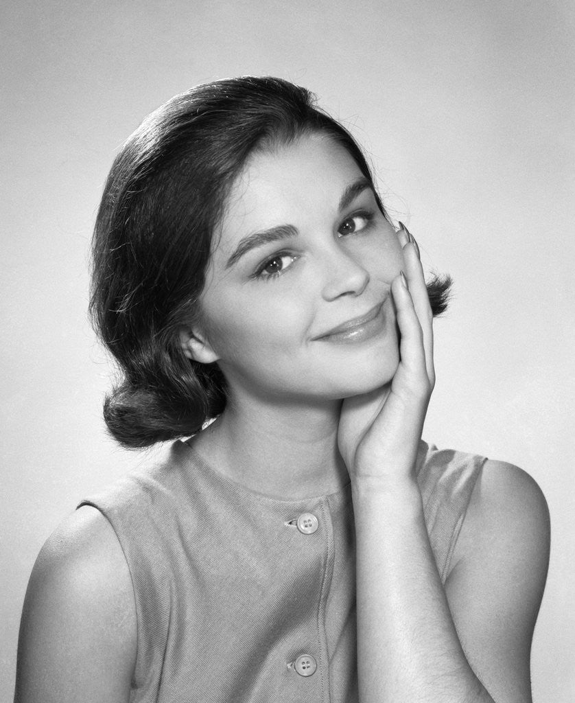 Detail of 1960s smiling brunette young woman hand to cheek facial expression gesture looking at camera by Anonymous