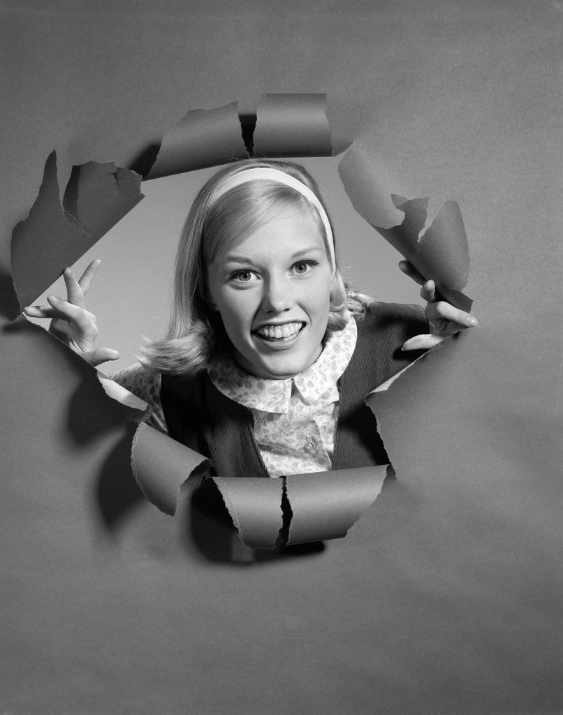 Detail of 1960s blond woman breaking through ripped paper looking at camera smiling wearing headband by Anonymous