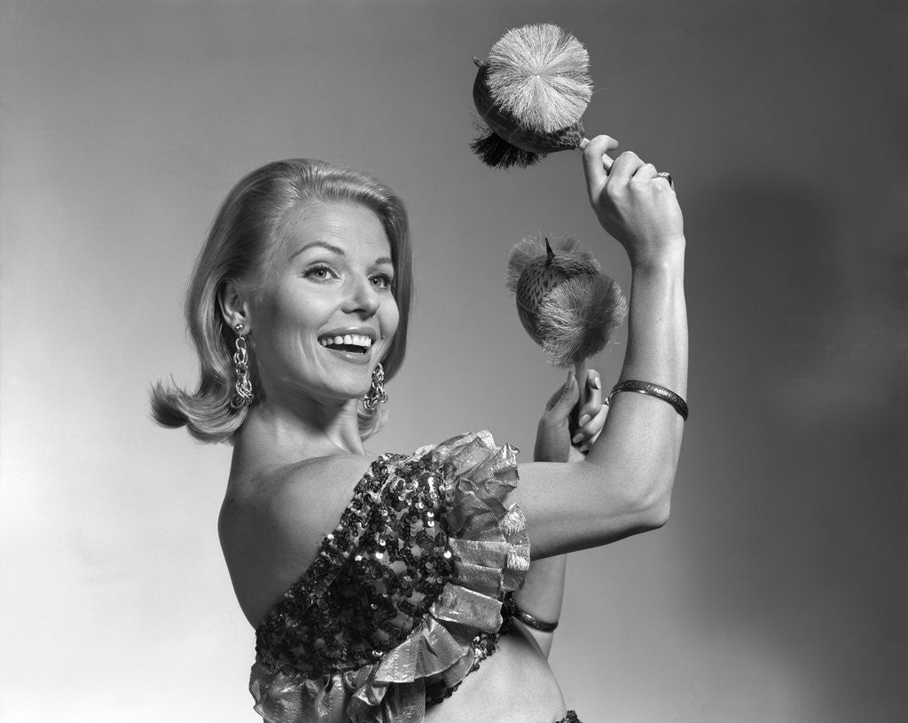 Detail of 1960s smiling blond woman looking at camera shaking noise makers in her hands wear ruffled halter top by Anonymous