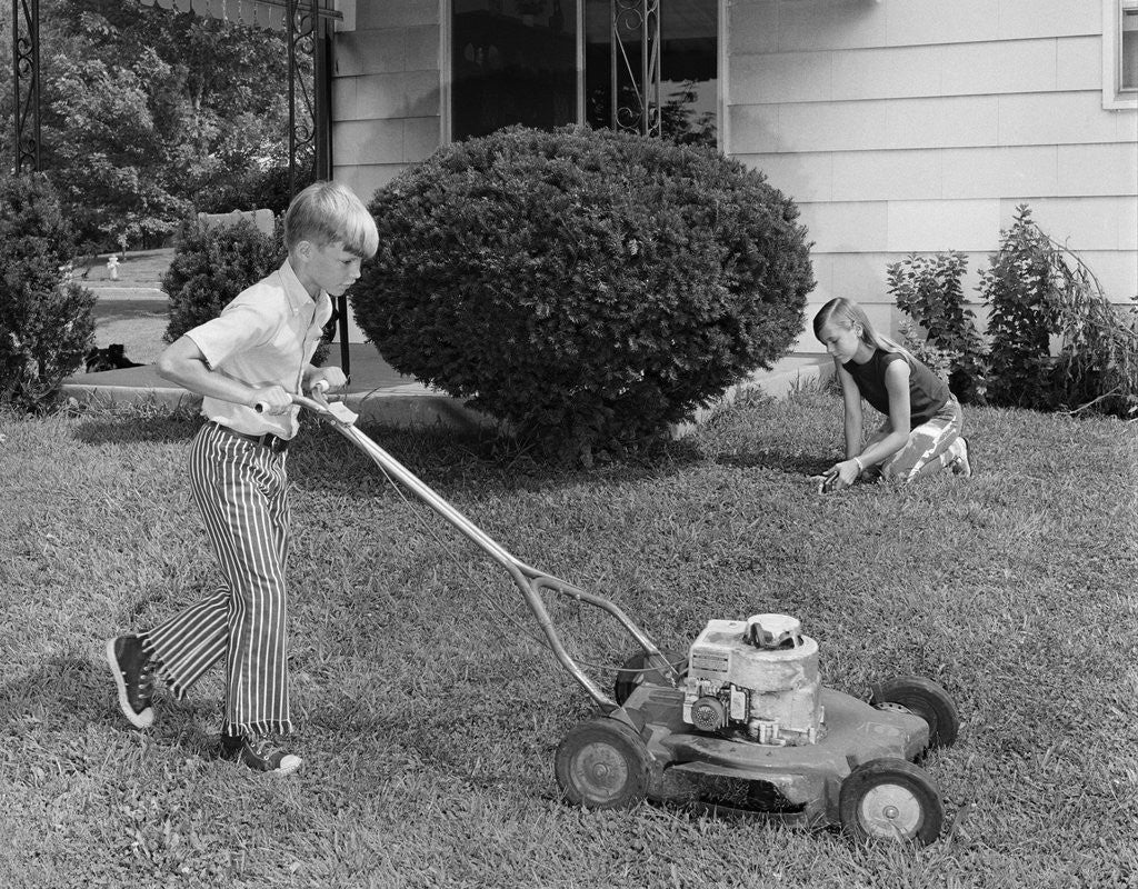 Detail of 1970s brother and sister doing chores mowing lawn cutting grass yard work together by Anonymous