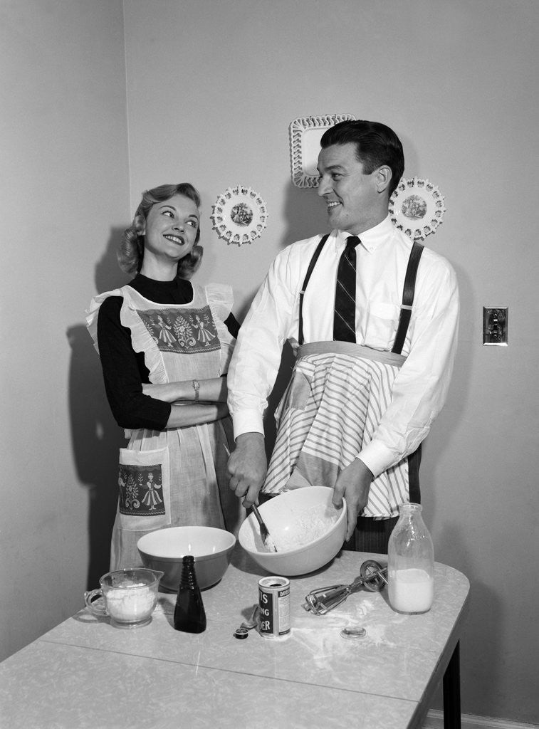 Detail of 1950s satisfied amused smiling couple husband wife in kitchen cooking together by Anonymous