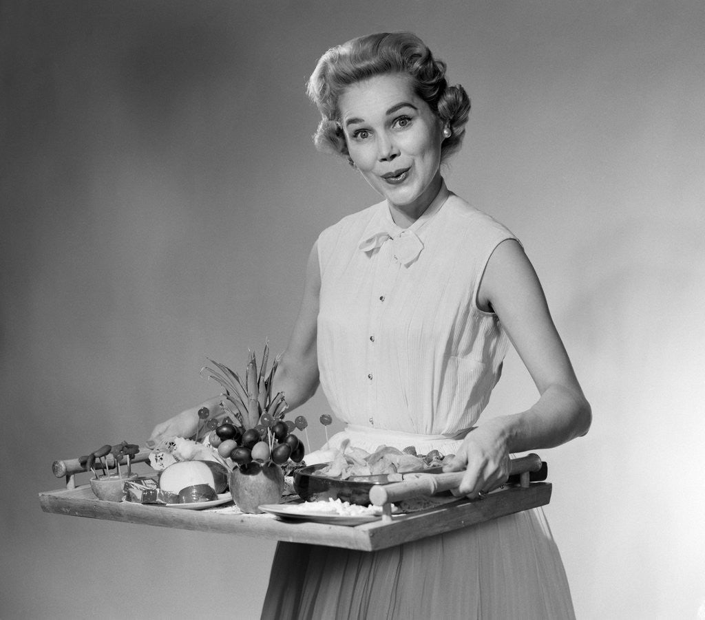 Detail of 1950s woman looking at camera smiling holding platter of hors d'oeuvres snacks by Anonymous