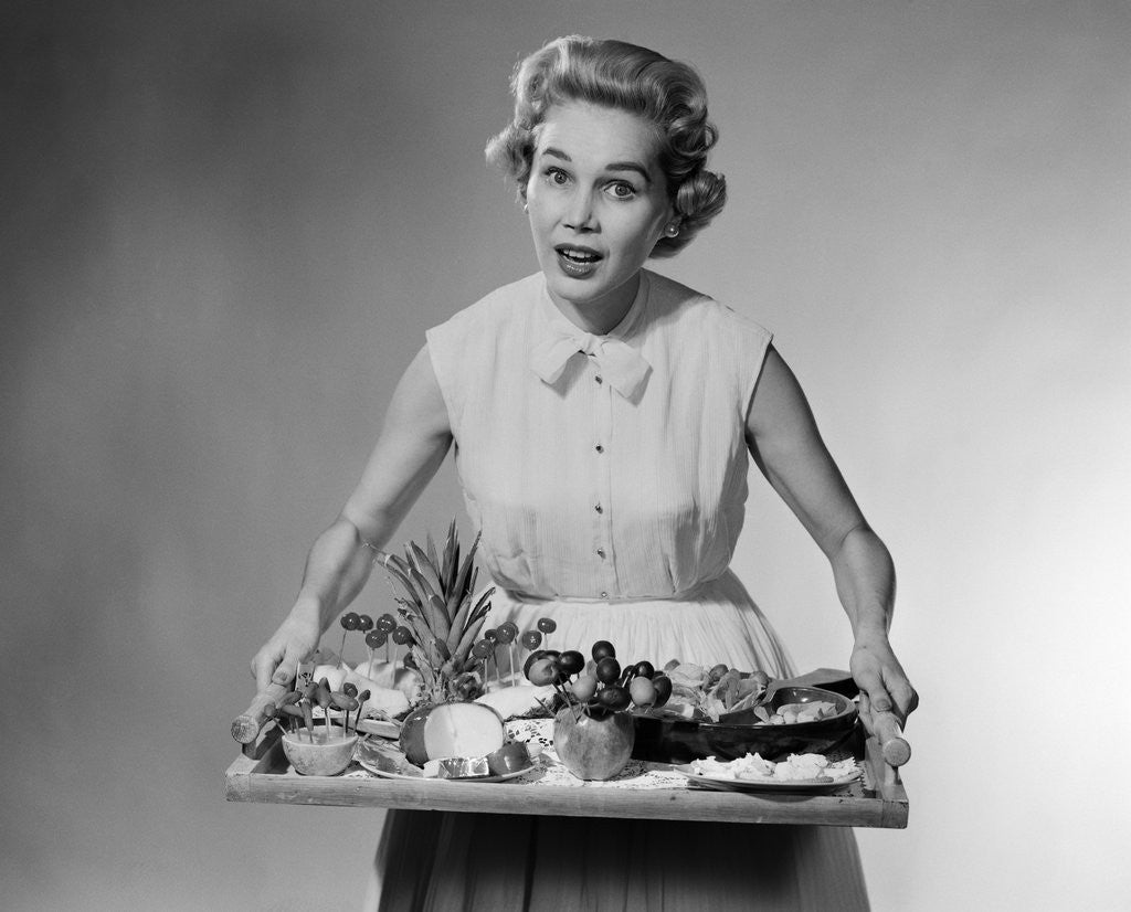 Detail of 1950s woman looking at camera speaking holding platter of hors d'oeuvres snacks by Anonymous