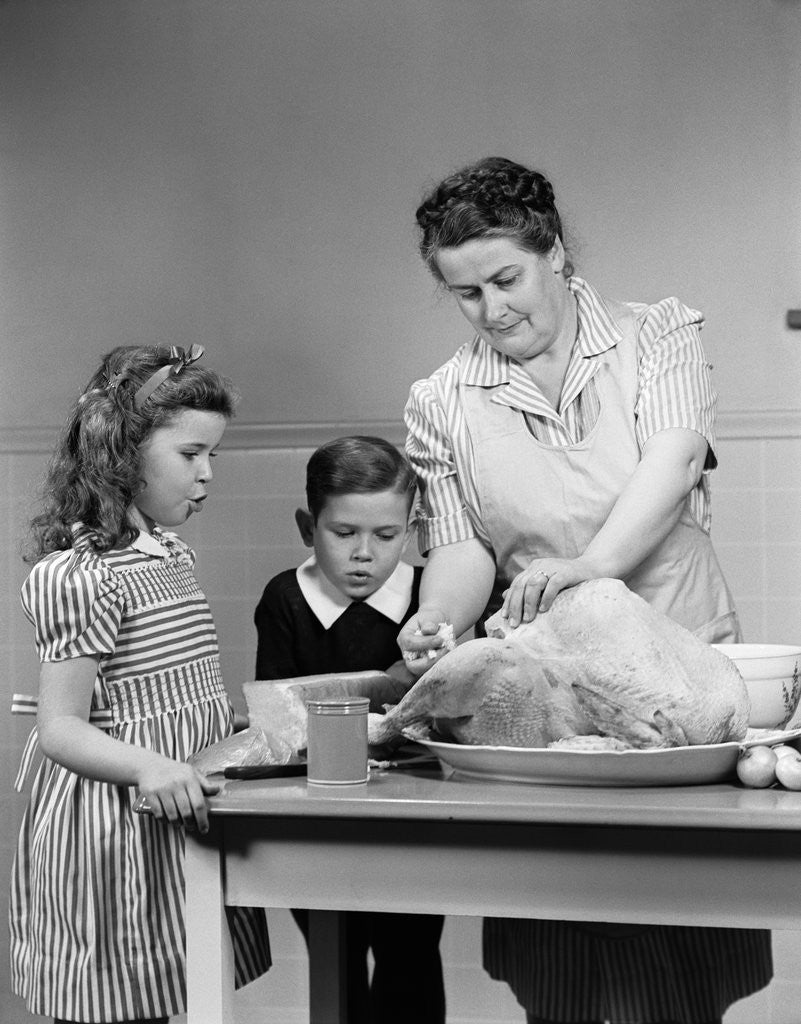 Detail of 1940s mother son daughter in kitchen stuffing turkey for thanksgiving dinner by Anonymous