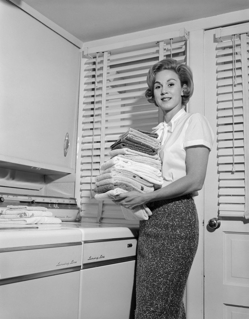 Detail of 1960s woman holding folded laundry looking at camera by Corbis