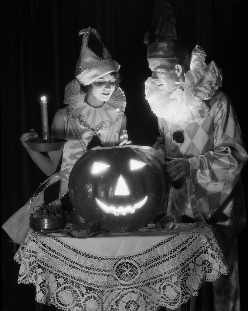 Detail of 1920s 1930s couple in costumes looking down into candle light from carved pumpkin jack-o-lantern by Corbis