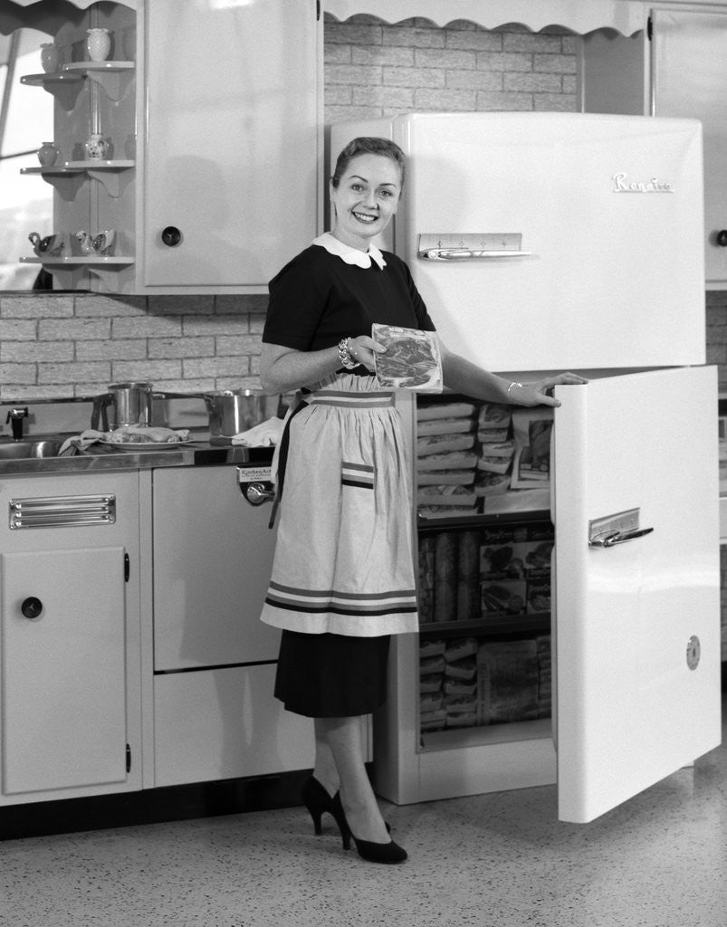 Detail of 1950s smiling woman housewife in kitchen taking frozen food out of refrigerator freezer by Anonymous