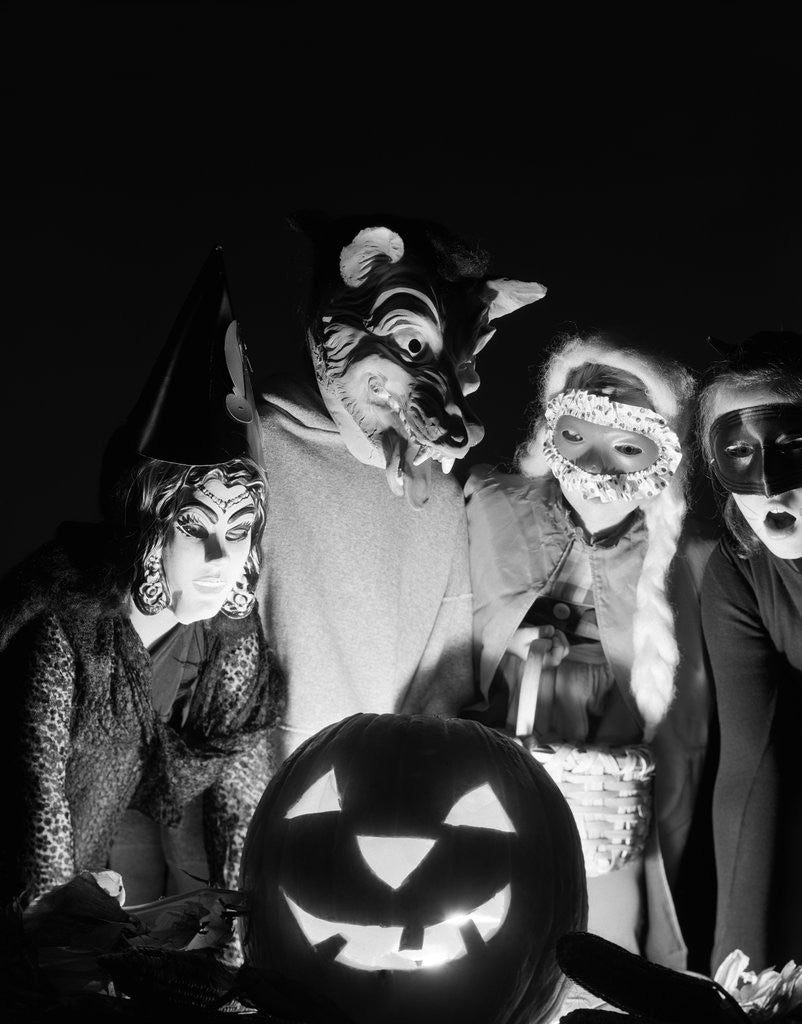 Detail of 1960s group of four children in halloween costumes gathered around jack-o'-lantern indoor by Corbis