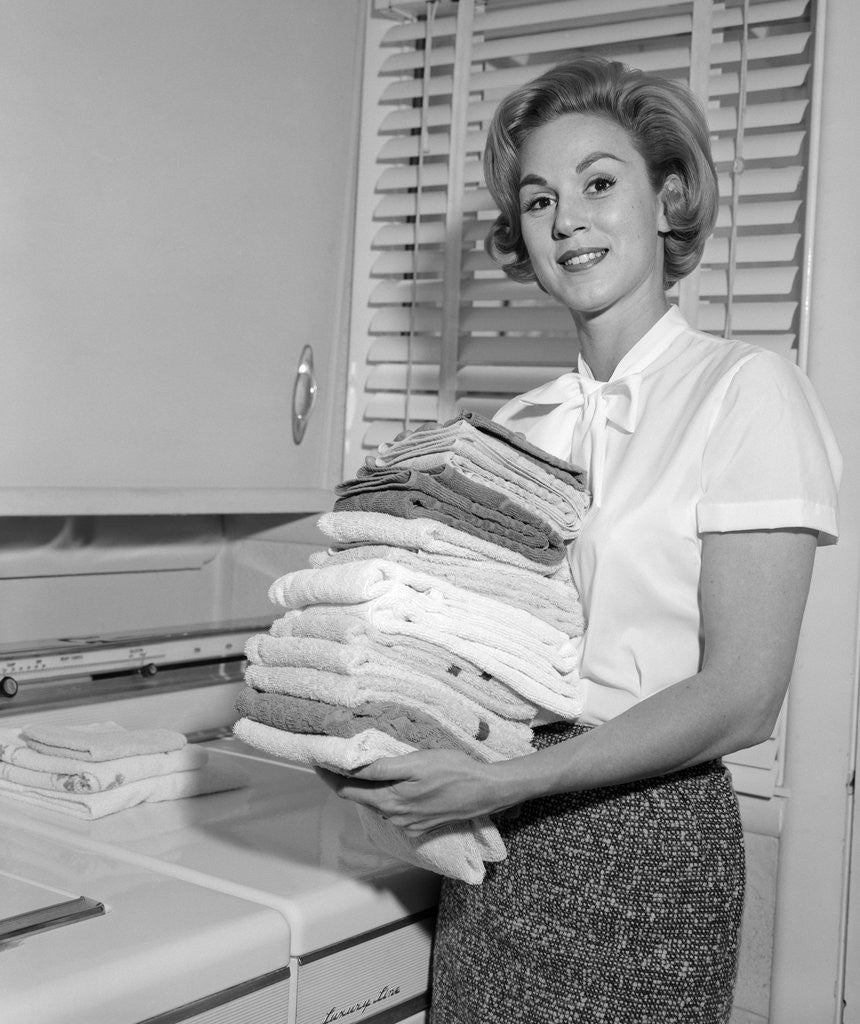 Detail of 1960s smiling woman holding folded laundry looking at camera by Anonymous