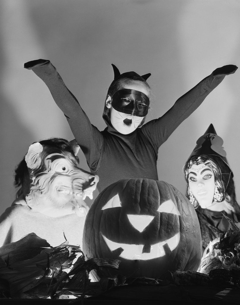 Detail of 1950s 3 children in costumes around a carved pumpkin jack-o-lantern by Anonymous