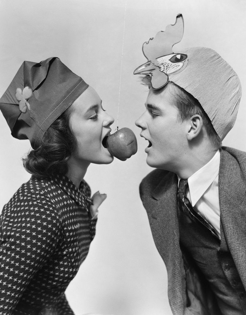 Detail of 1940s couple teen boy and girl wearing party hats bobbing for an apple on a string by Anonymous