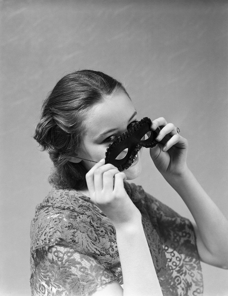 Detail of 1930s 1940s woman putting on taking off black eye mask by Corbis