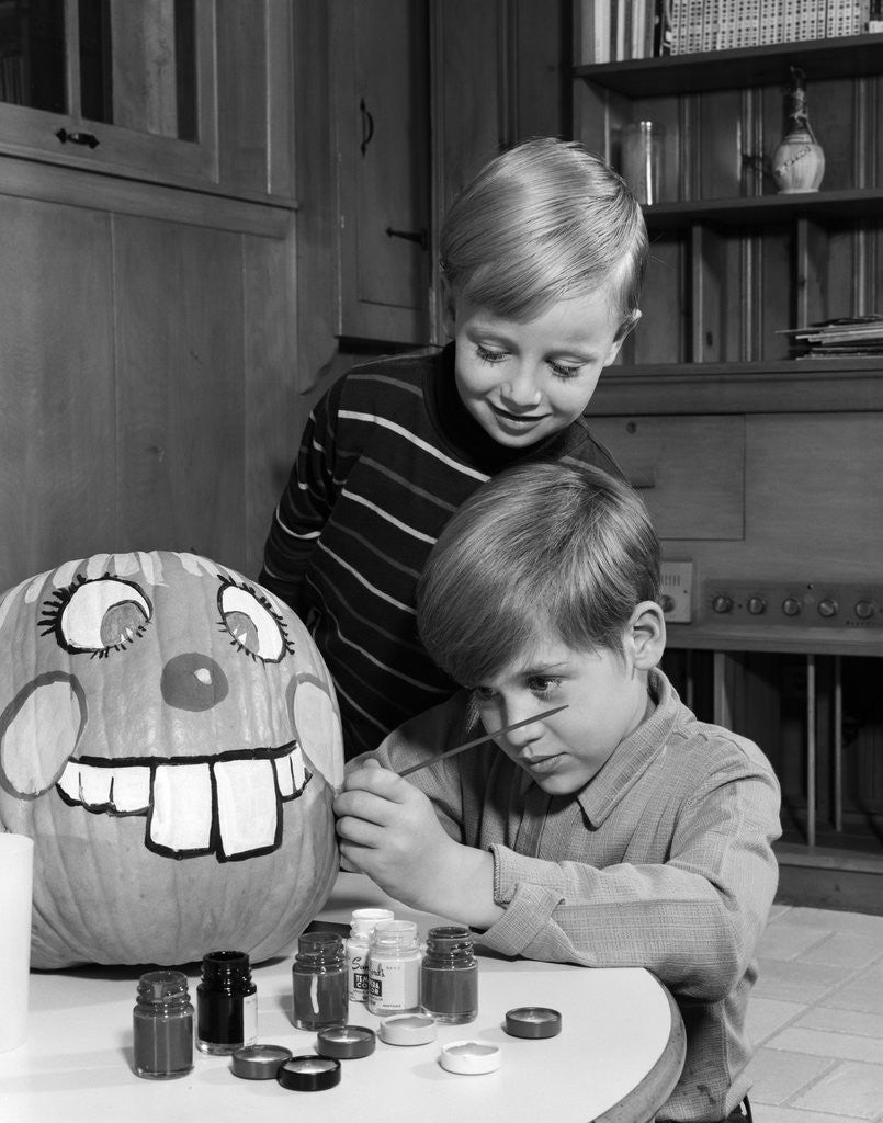 Detail of 1960s two boys brothers painting jack-o'-lantern face on pumpkin by Anonymous