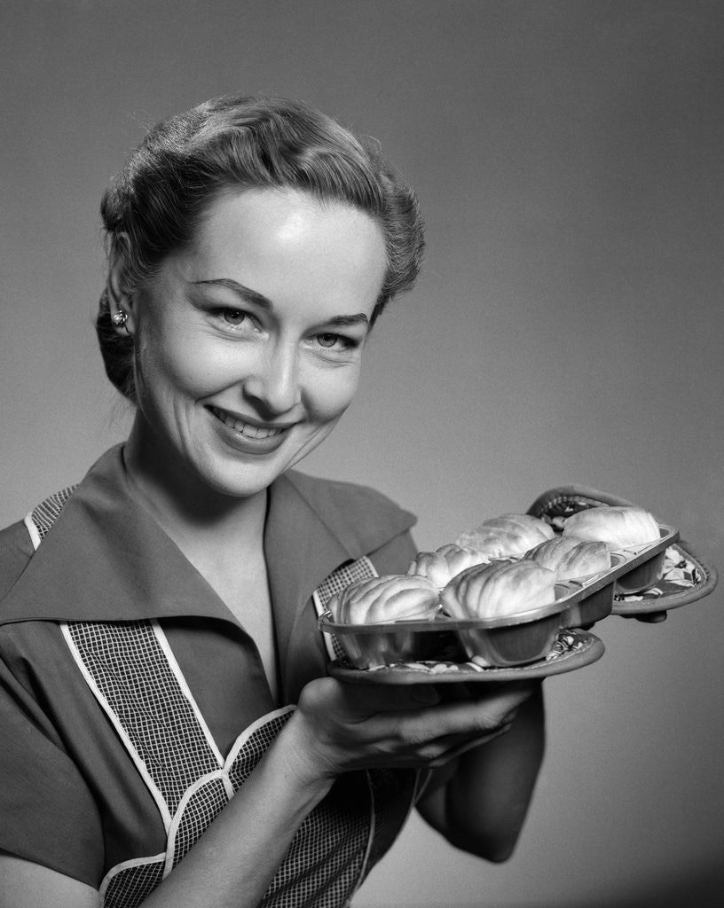 Detail of 1950s smiling woman holding freshly baked rolls looking at camera by Anonymous