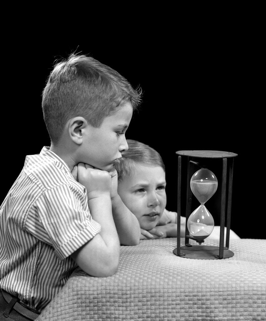 Detail of 1940s two boys waiting watching sand falling in hourglass by Corbis